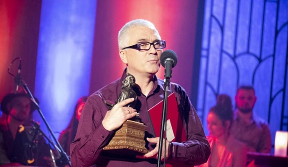 jeden z laureatów stojący z dyplomem i statuetką, przemawia do mikrofonu
