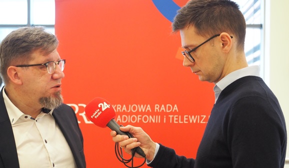 Przewodniczący KRRiT udziela wywiadu. W tel czerwony baner z logiem KRRiT